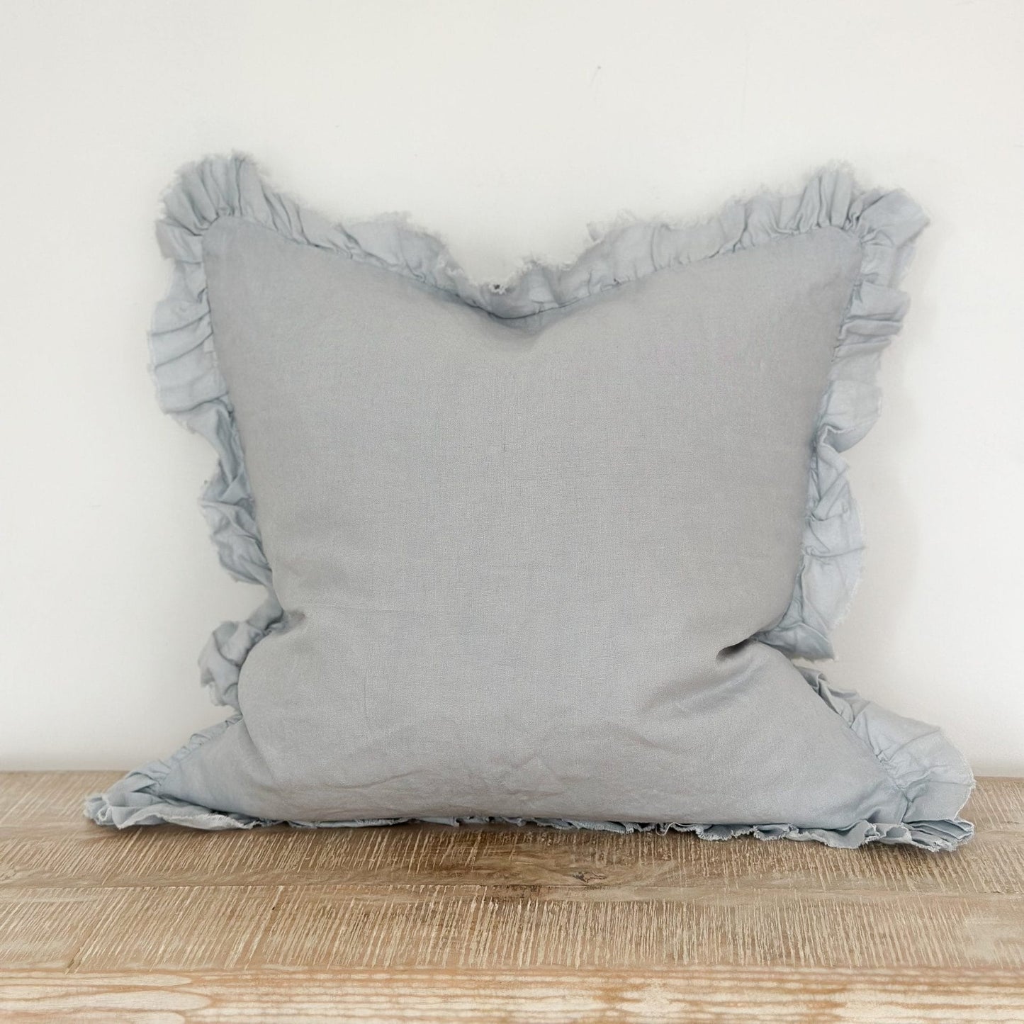 pale blue pillow with ruffled edges on a wooden surface