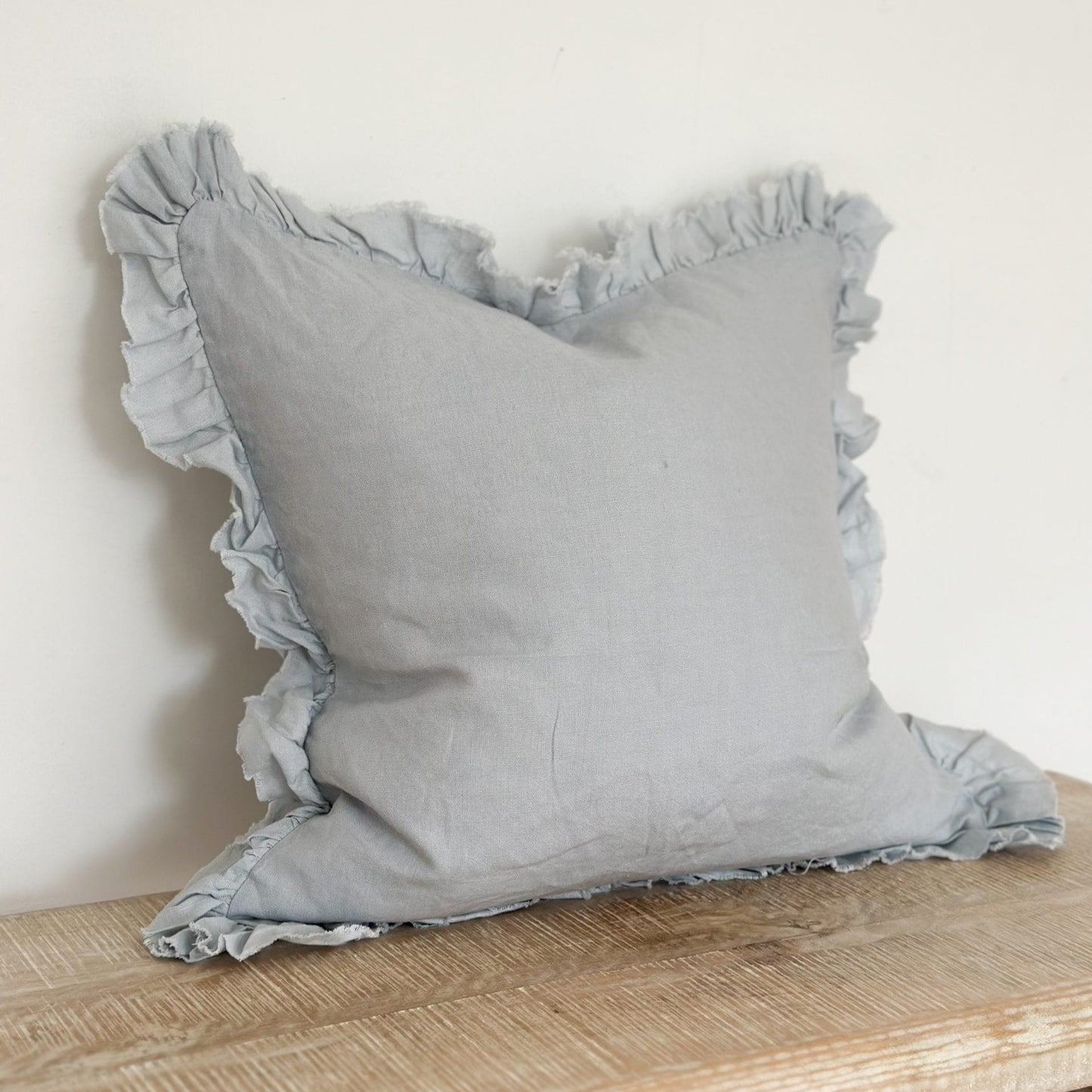 Pale blue pillow with ruffled edges on a wooden surface against a white background