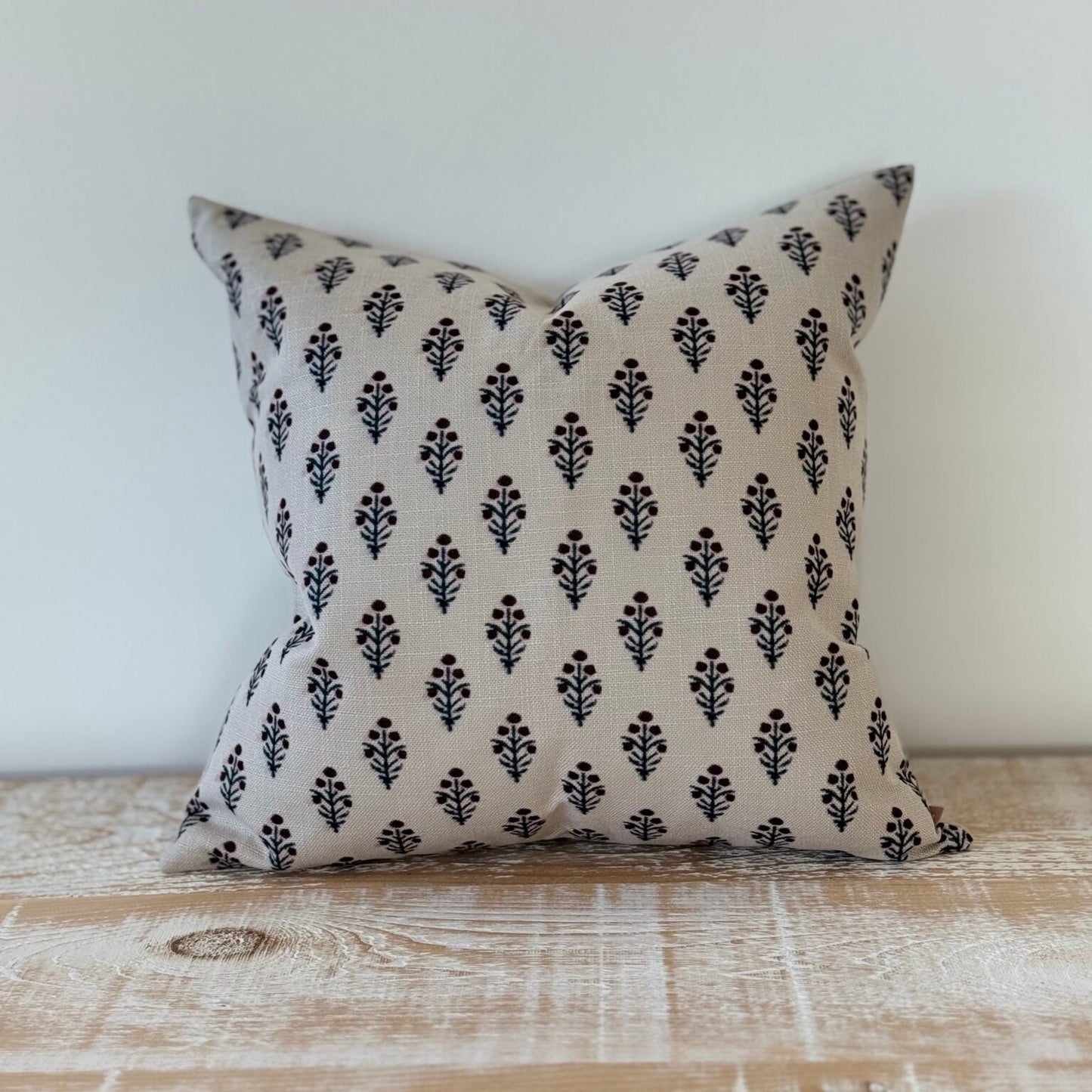 Decorative pillow with black pattern on beige fabric, placed on a wooden surface.