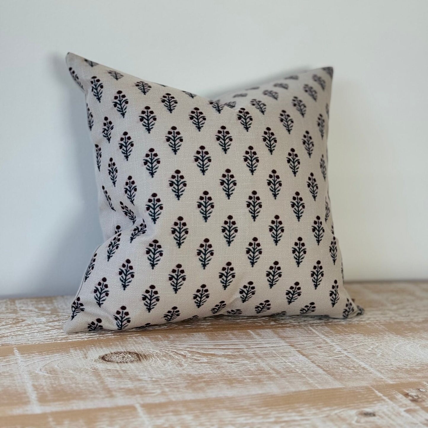 Decorative pillow with black floral pattern on a beige background, placed on a wooden surface.
