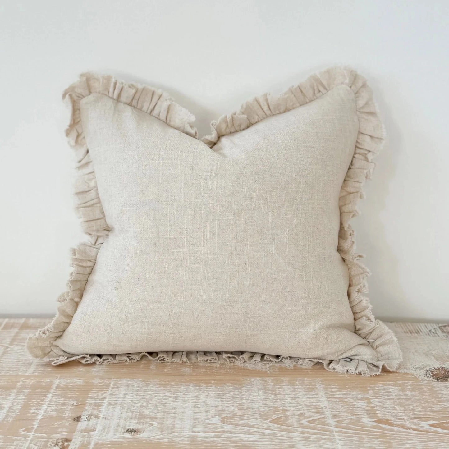 Cream pillow with ruffled edges on a wooden surface.