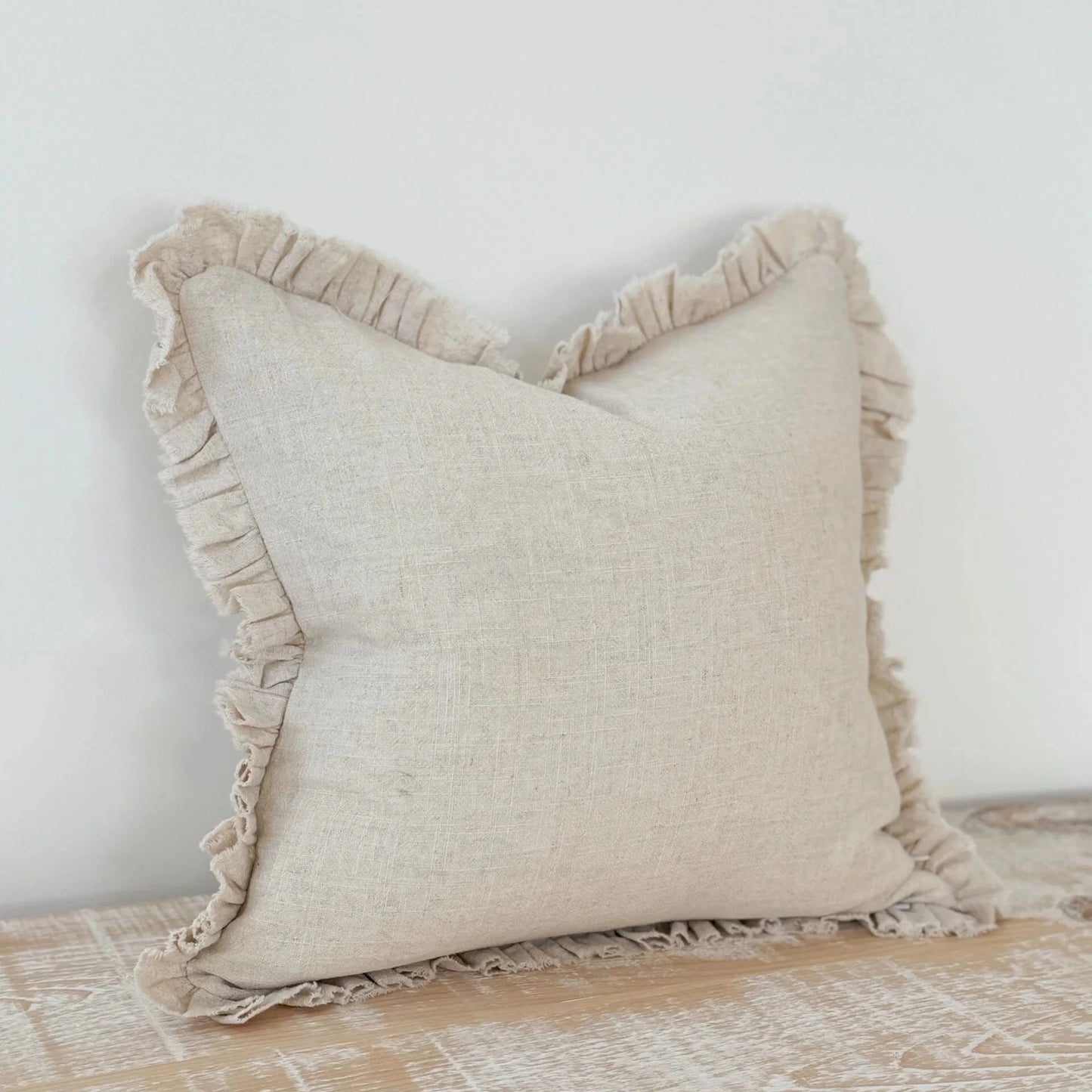 A cream cushion with ruffle detailing on a wooden surface.