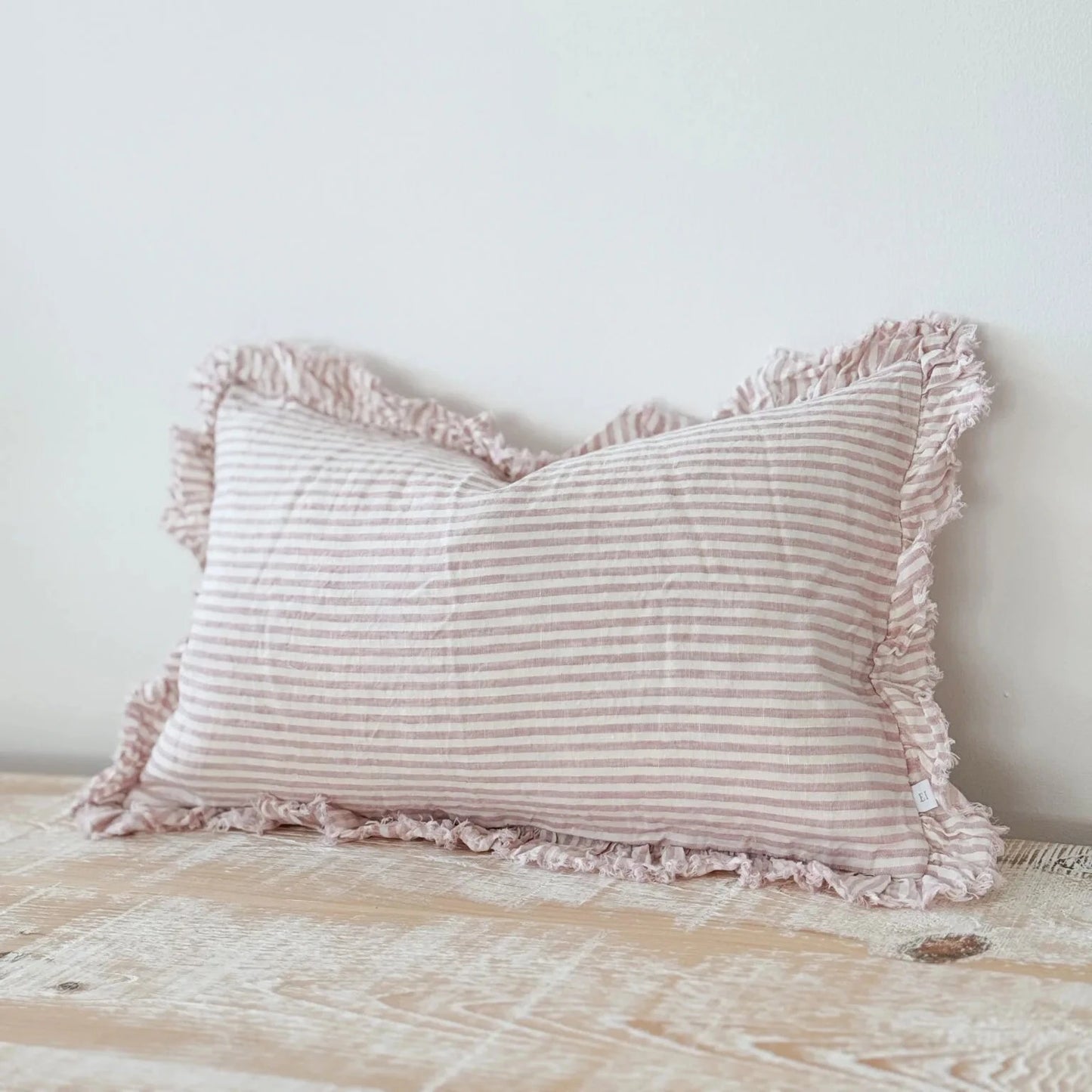 Striped pillow with fringes on a wooden surface.