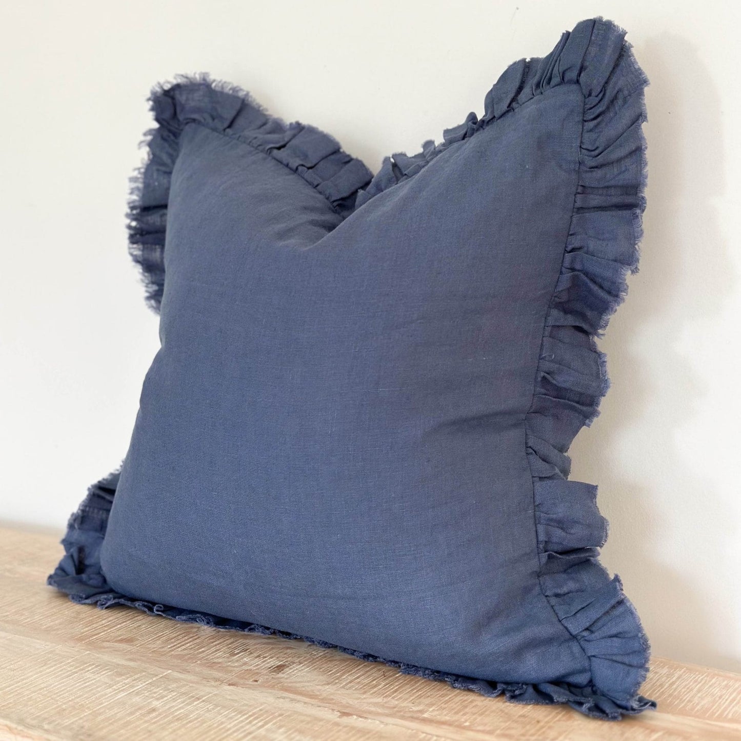 Blue pillow with ruffles on a wooden surface against a white background
