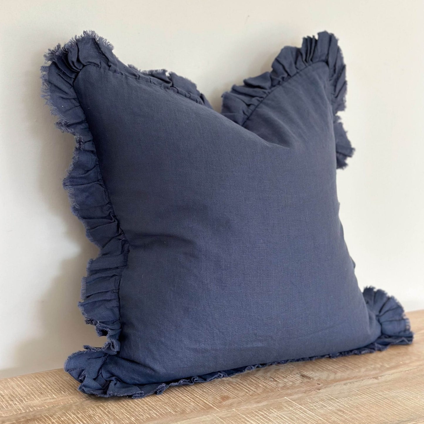 Navy blue pillow with ruffled edges on a wooden surface against a light background