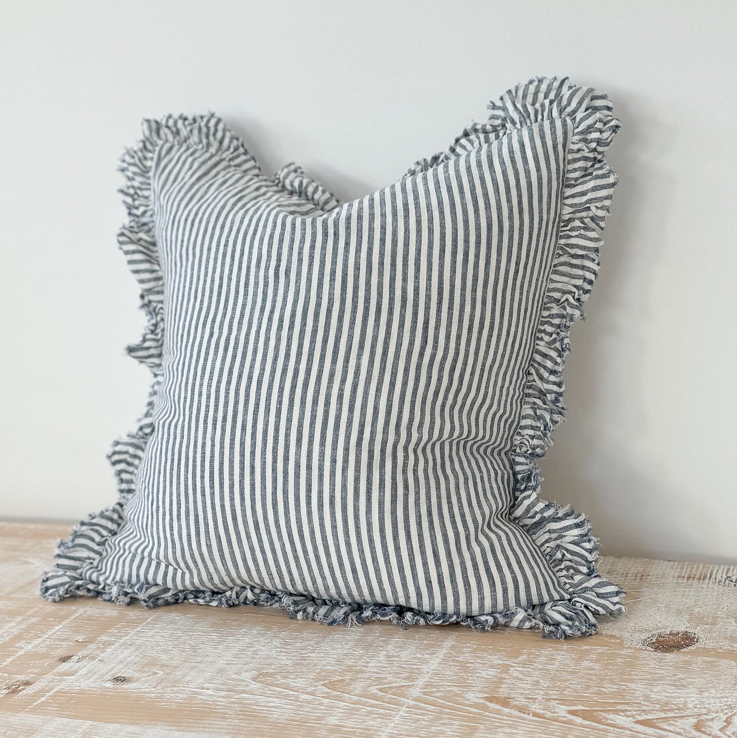 Striped pillow with tassels on a wooden surface and light gray background