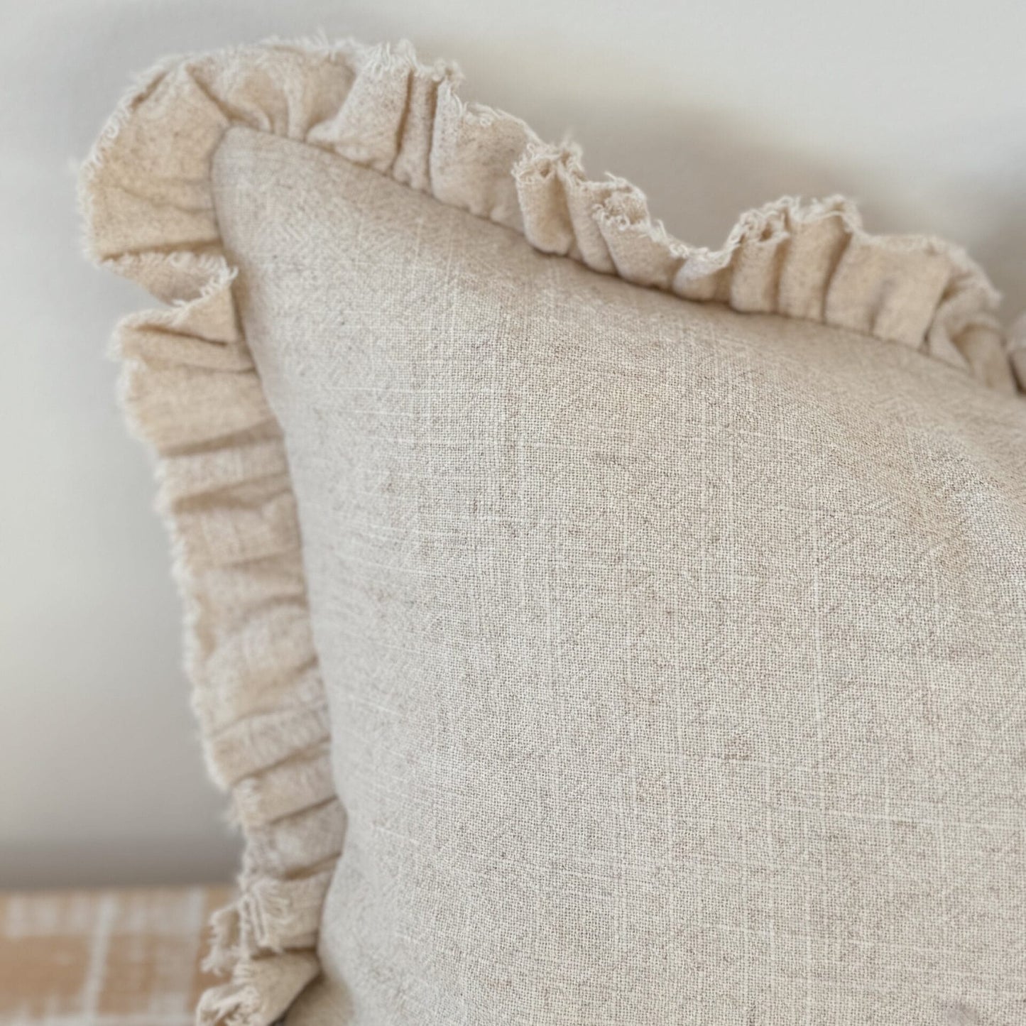 Beige pillow with ruffled edge on a neutral background