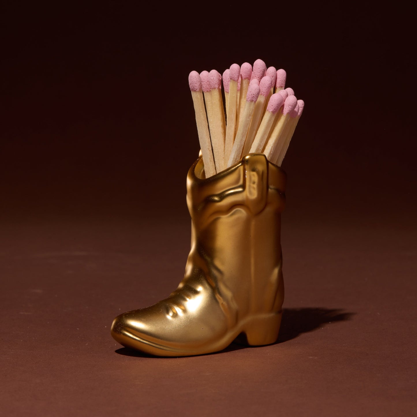 Gold boot-shaped matchbox with matches on a brown background