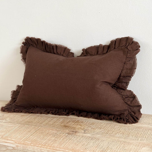 Brown ruffled pillow on a wooden surface with a white background