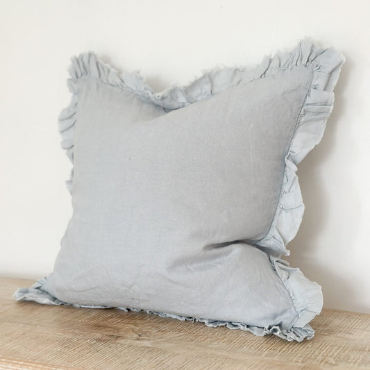 Light blue pillow with ruffled edges on a wooden surface