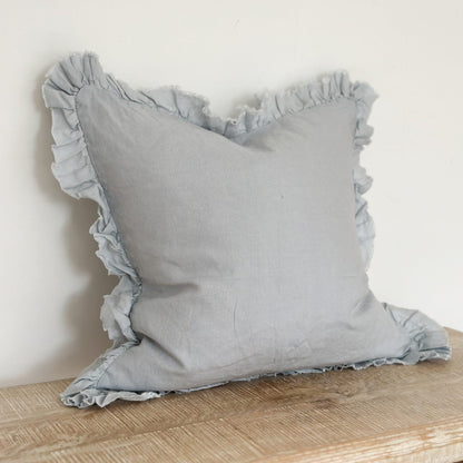 Pale blue pillow with ruffled edges on a wooden surface against a white background