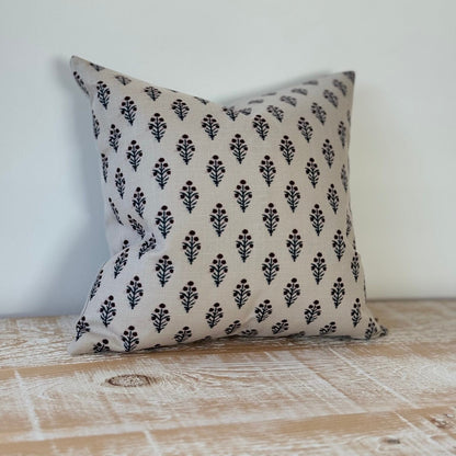 Decorative pillow with black floral pattern on a beige background, placed on a wooden surface.