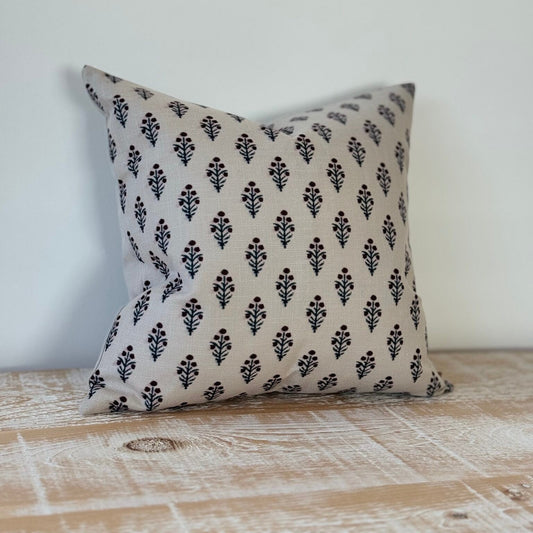 Decorative pillow with black floral pattern on a beige background, placed on a wooden surface.