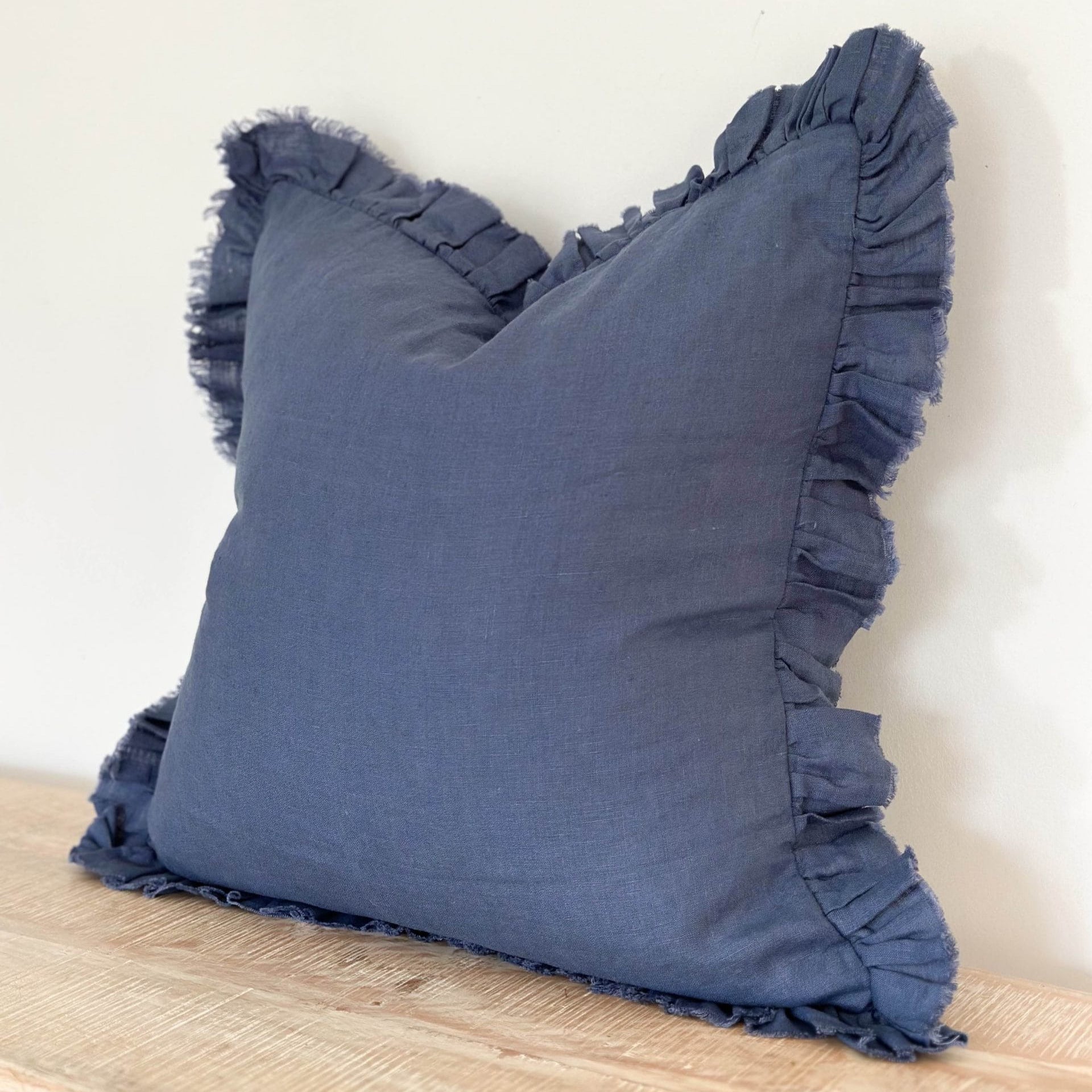 Blue pillow with ruffles on a wooden surface against a white background