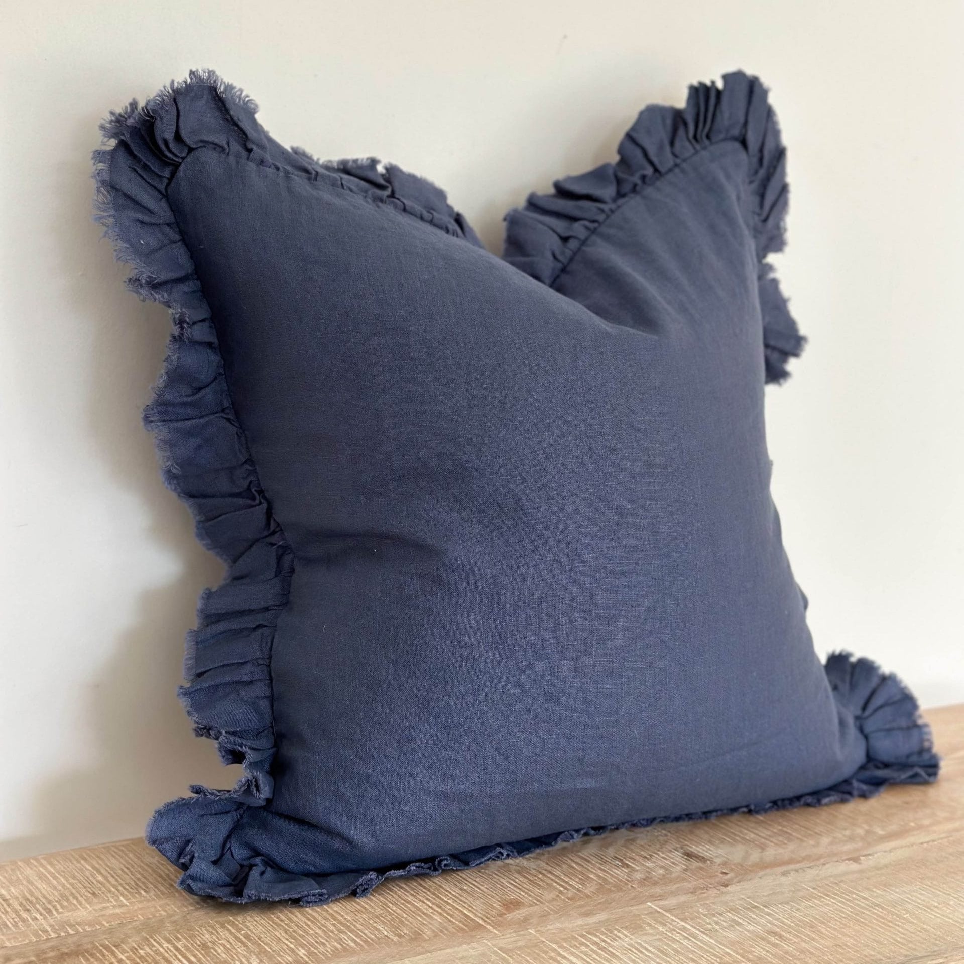 Navy blue pillow with ruffled edges on a wooden surface against a light background