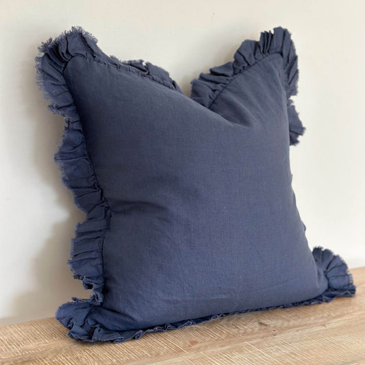 Navy blue pillow with ruffled edges on a wooden surface against a light background