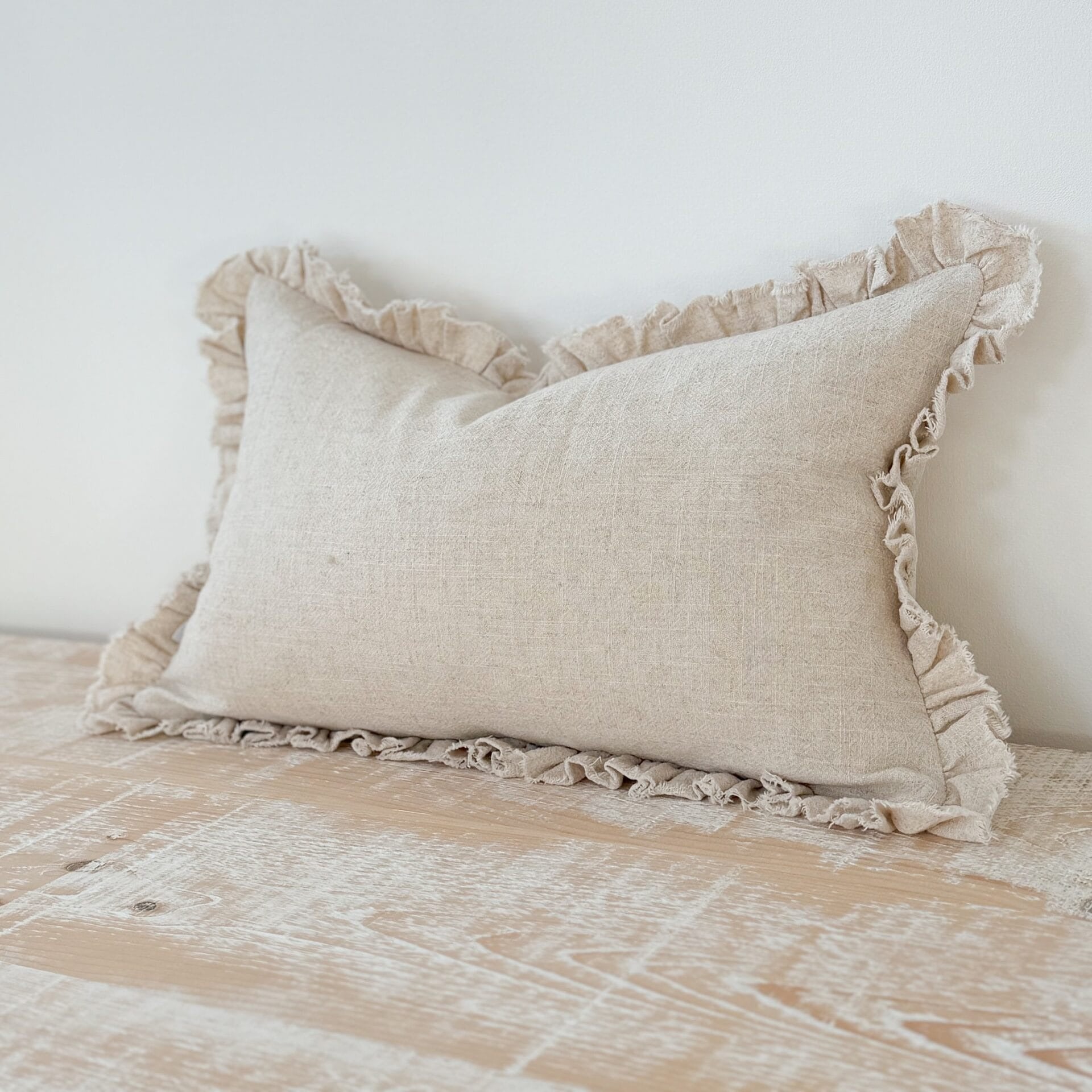 Beige pillow with ruffled edges on a bed against a white wall