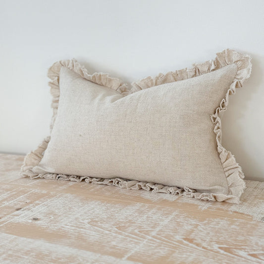 Beige pillow with ruffled edges on a bed against a white wall